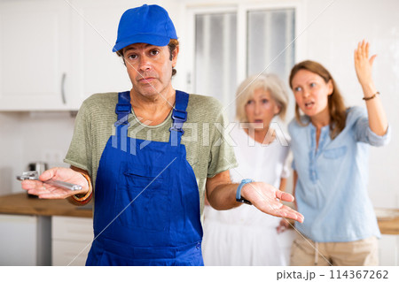 Inept plumber throws up his hands. In background, disgruntled apartment owners scold him Inept plumber throws up his hands. In background, disgruntled apartment owners scold him 114367262