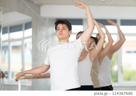 Guy performing third position at barre during group ballet class Guy performing third position at barre during group ballet class 114367680
