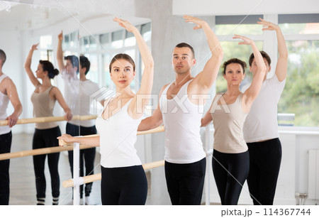 Group of positive young women and men engaged in classical ballet in dance studio performs exercise standing in 3rd position of ballet stance 114367744