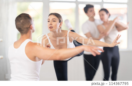 Portrait of positive young man and female partner training ballet pose with group of guys and girls in dance class Portrait of positive young man and female partner training ballet pose with group of guys and girls in dance class 114367795