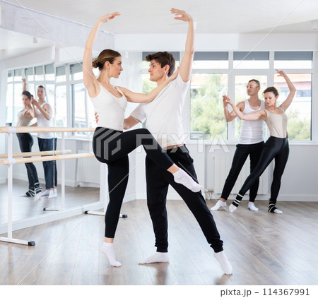 Happy smiling woman dressed in black and white sportswear enjoying ballet choreography with male partner during group class in dance salon Happy smiling woman dressed in black and white sportswear enjoying ballet choreography with male partner during group class in dance salon 114367991