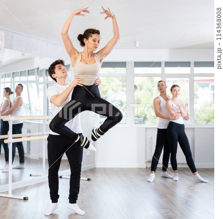 Contemporary ballet dancers couple performing graceful choreography, training entrechat ballet pose in ballet hall Contemporary ballet dancers couple performing graceful choreography, training entrechat ballet pose in ballet hall 114368008