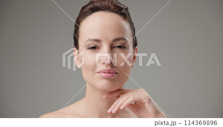 Beauty, health, cosmetics, anti-aging therapy and skin care concept - young beautiful brunette Caucasian woman touching face and looking at camera Beauty, health, cosmetics, anti-aging therapy and skin care concept - young beautiful brunette Caucasian woman touching face and looking at camera 114369896