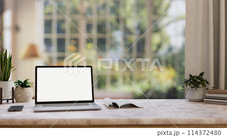 Home office workspace, a white-screen laptop computer mockup on a table in a comfortable room. 114372480