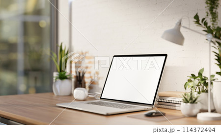 A minimalist workspace features a laptop computer mockup on a desk against the white brick wall. 114372494