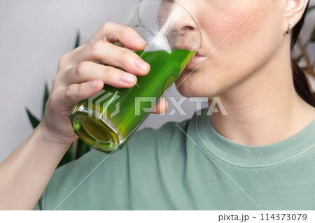 Woman Drinks green wheatgrass energy shake. close up Woman Drinks green wheatgrass energy shake. close up 114373079