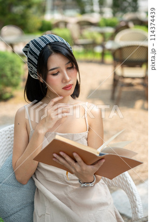 A beautiful Asian woman in a cute dress relaxes in a beautiful garden, reading a book. A beautiful Asian woman in a cute dress relaxes in a beautiful garden, reading a book. 114374439