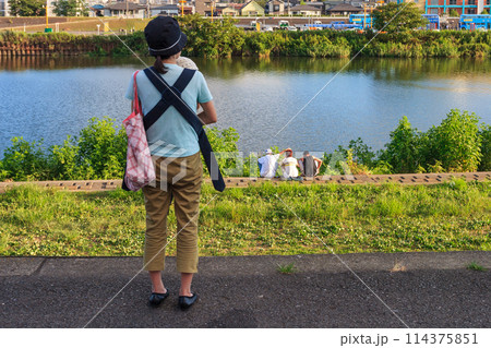 土手の上で赤ちゃんを抱っこする母親と川岸に座り雑談をする人達 土手の上で赤ちゃんを抱っこする母親と川岸に座り雑談をする人達 114375851