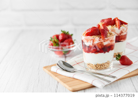 Homemade layered dessert with strawberries yogurt granola strawberry jam in glasses.  114377019
