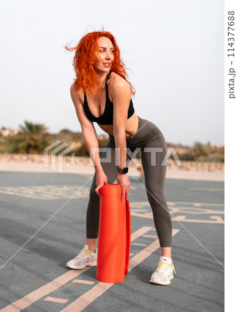 Redhead woman athlete with rolled yoga mat at Redhead woman athlete with rolled yoga mat at 114377688