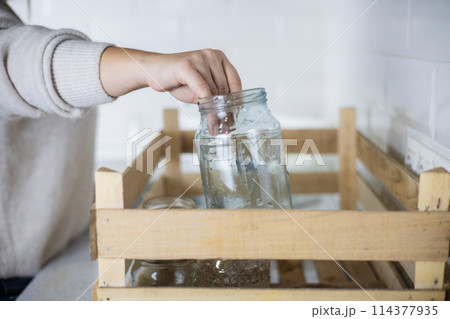 A woman wants to send washed glass jars for recycling and puts them in a drawer in the kitchen. An eco activist sorts garbage at home, taking care of environmental pollution. Garbage recycling. A woman wants to send washed glass jars for recycling and puts them in a drawer in the kitchen. An eco activist sorts garbage at home, taking care of environmental pollution. Garbage recycling. 114377935