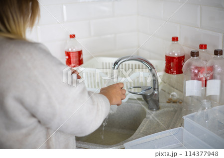 A woman standing with her back is washing a plastic bottle in the sink A woman sorts plastic in the kitchen of her home for recycling. Concept of eco-friendly lifestyle plastic recycling world trend. 114377948