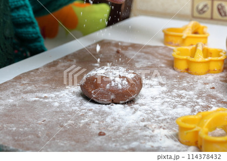 A woman sprinkles a lump of dough with flour before rolling it out. Near plastic mold and rolling pin. Cooking gingerbread. A woman sprinkles a lump of dough with flour before rolling it out. Near plastic mold and rolling pin. Cooking gingerbread. 114378432