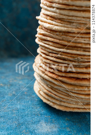 Flatbread lavash, chapati, naan, heap of tortilla on a blue background Homemade flatbread stacked. Flatbread lavash, chapati, naan, heap of tortilla on a blue background Homemade flatbread stacked. 114378874