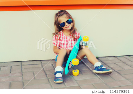 Stylish little girl child posing with skateboard on city street 114379391