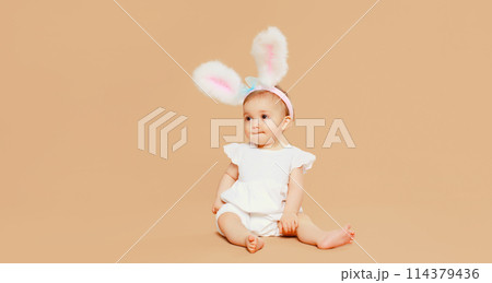 Portrait cute baby with easter rabbit ears sitting on brown studio background 114379436