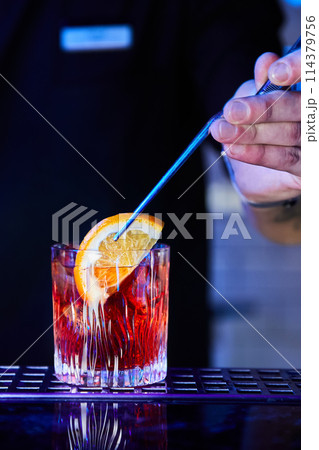 The bartender dips an orange slice into a prepared alcoholic cocktail 114379756