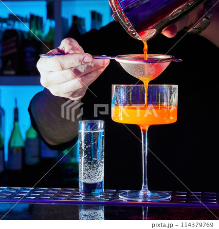 The bartender prepares a cocktail Is Love on the bar counter using a shaker and a strainer The bartender prepares a cocktail Is Love on the bar counter using a shaker and a strainer 114379769