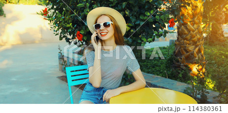 Happy young woman calling on mobile phone sitting on the table in street cafe 114380361