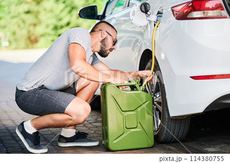 Suspicious man stealing gasoline from car tunk. Thief trying to pump fuel from someone else's automobile. Stealing fuel in broad daylight. Suspicious man stealing gasoline from car tunk. Thief trying to pump fuel from someone else's automobile. Stealing fuel in broad daylight. 114380755