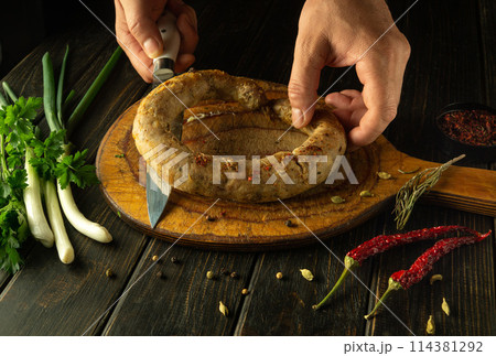 Cooking homemade sausage on the kitchen table. Man hands with a knife before slicing meat sausage for lunch 114381292