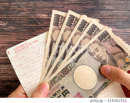 通帳と5万円を持つ女性の手元 114381352