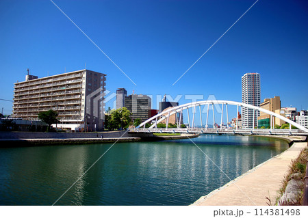青空下の小倉リバーウォークと紫川に掛かる橋 114381498