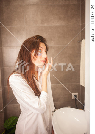 Young woman cleansing face in bathroom with skincare routine. 114382124