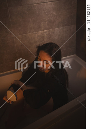 Upset woman sitting with arms wrapped around legs in tub. Upset woman sitting with arms wrapped around legs in tub. 114382136