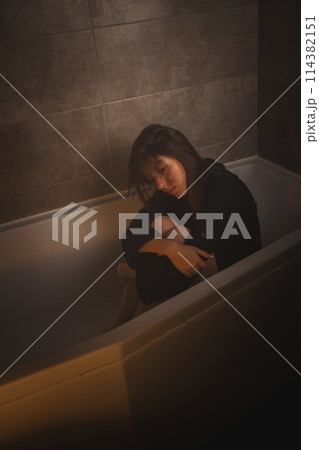 Sad woman sitting with knees drawn up in tub. Sad woman sitting with knees drawn up in tub. 114382151