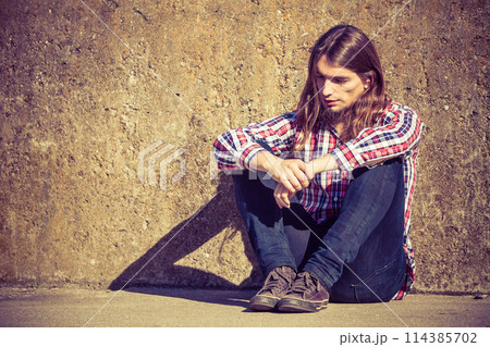Man long haired sitting alone sad on grunge wall Man long haired sitting alone sad on grunge wall 114385702