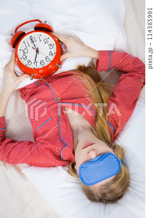 Sleeping woman wearing pajamas holding clock Sleeping woman wearing pajamas holding clock 114385991