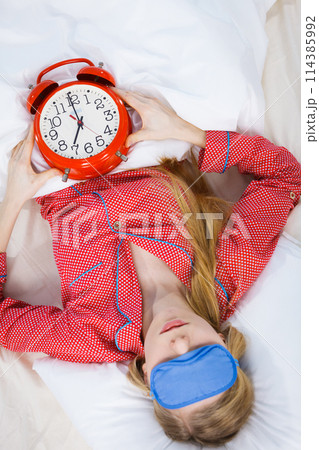 Sleeping woman wearing pajamas holding clock Sleeping woman wearing pajamas holding clock 114385992