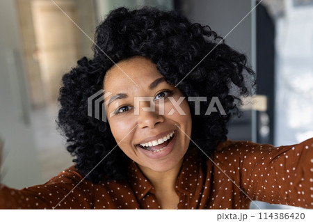 A young, cheerful woman with curly hair captures a happy moment with a selfie in a stylish, well-lit interior. Her expression is vibrant and engaging. A young, cheerful woman with curly hair captures a happy moment with a selfie in a stylish, well-lit interior. Her expression is vibrant and engaging. 114386420