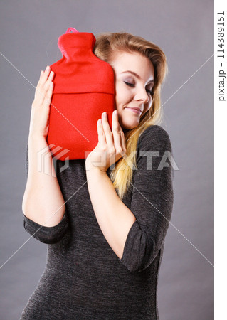 Woman hugs hot water bottle in red fleece cover 114389151