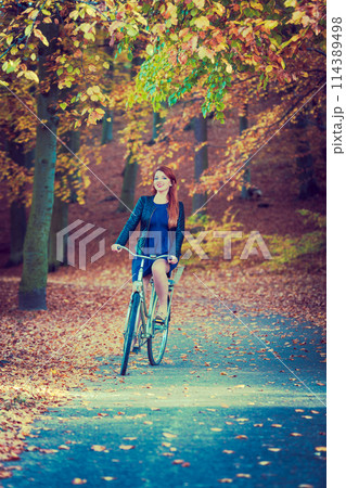 Redhead lady cycling in park. Redhead lady cycling in park. 114389498