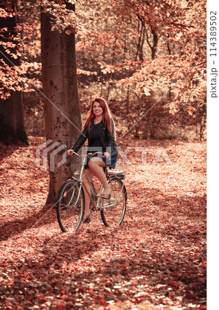Redhead lady cycling in park. 114389502