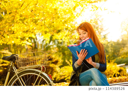 woman girl relaxing in autumnal park reading book 114389526