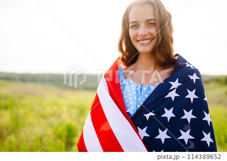 Young woman proudly hold waving american USA flag on blooming meadow. 4th of July. Independence Day. 114389652