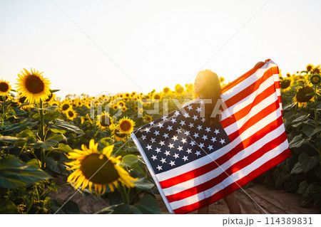 Woman proudly hold waving american USA flag in in the sunflower field. Independence Day, 4th July. 114389831