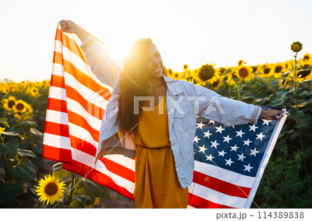 Woman proudly hold waving american USA flag in in the sunflower field. Independence Day, 4th July. Woman proudly hold waving american USA flag in in the sunflower field. Independence Day, 4th July. 114389838