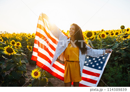 Woman proudly hold waving american USA flag in in the sunflower field. Independence Day, 4th July. Woman proudly hold waving american USA flag in in the sunflower field. Independence Day, 4th July. 114389839