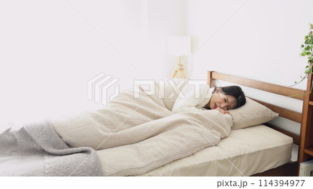 布団の中で寒気を感じる女性 114394977