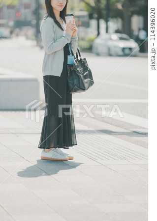 オフィス街で信号待ちをするシアースカートにスニーカーの若い働く女性 114396020