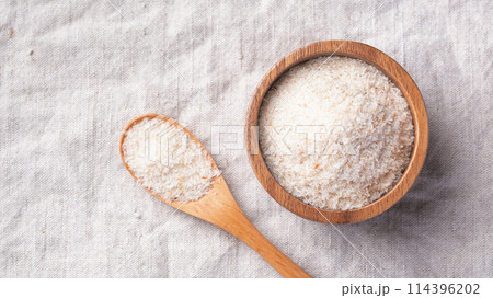 Psyllium husk in wood bowl with spoon on linen table cloth background, top view, copy space 114396202