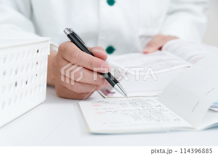 お薬手帳で薬の確認をしている調剤薬局の薬剤師の手元 お薬手帳で薬の確認をしている調剤薬局の薬剤師の手元 114396885