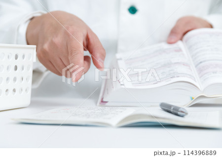 お薬手帳の薬をマニュアルを見て安全確認をする薬剤師の手元 114396889