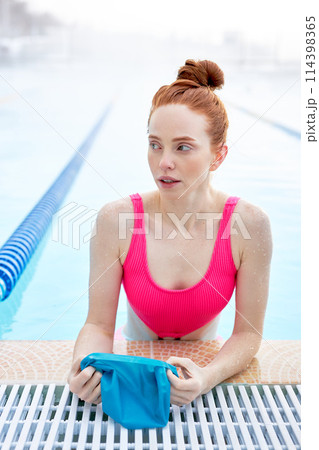 Pretty awesome ginger woman putting on swim cap at the pool 114398365