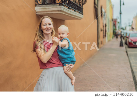 Mother and baby son tourists explore the vibrant streets of Valladolid, Mexico, immersing herself in the rich culture and colorful architecture of this charming colonial town 114400210