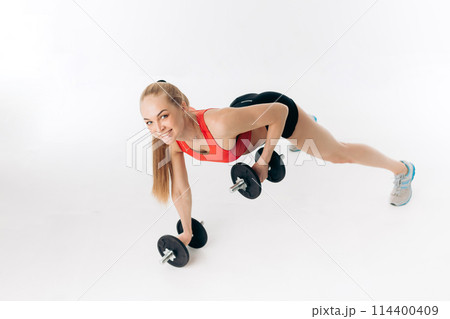sporty woman doing press ups with dumbbells in the gym 114400409